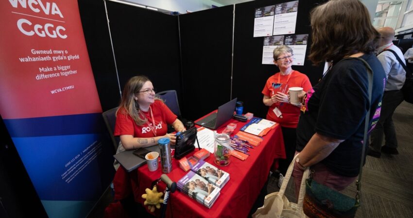 Two exhibitors at a booth with red tablecloth and promotional items.