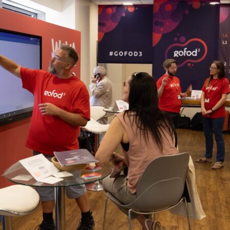 Group of exhibitors in red shirts posing near event signage.