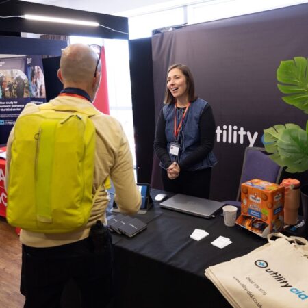 Exhibitor speaking to attendee wearing a yellow jacket at a booth.