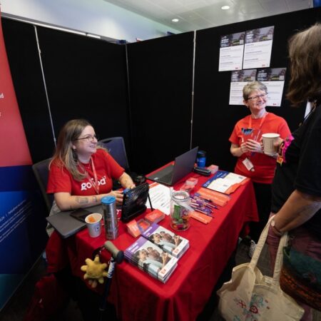 Two exhibitors at a booth with red tablecloth and promotional items.