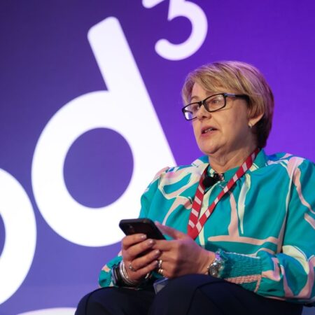 Individual in wheelchair on stage holding a microphone in front of event branding.