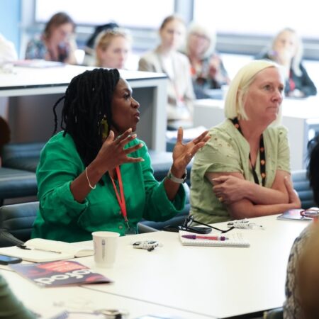 Two participants seated at a table engaged in conversation with documents.