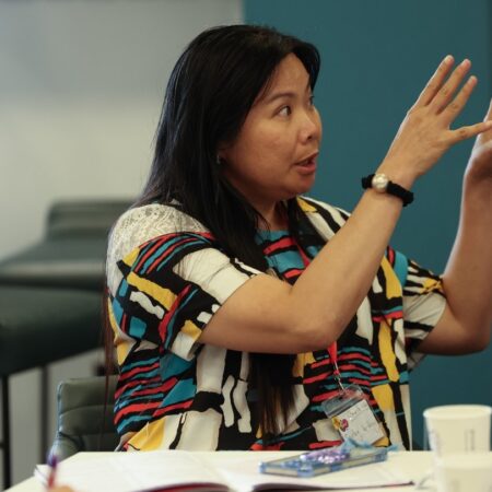 Participant gesturing with hands during a discussion at a table.