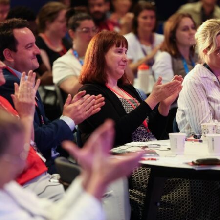 Audience clapping in a conference setting, some smiling.