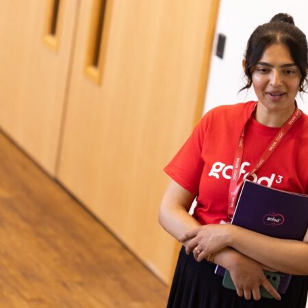 Person standing near a wooden wall wearing an event lanyard.