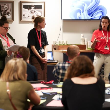 Group of participants around a table engaged in discussion, some wearing red event lanyards.
