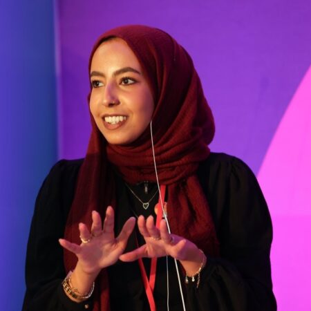 Attendee wearing a red headscarf speaking, using hand gestures to emphasize points.