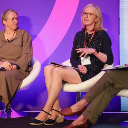 Two panelists seated on stage, speaking to an audience.