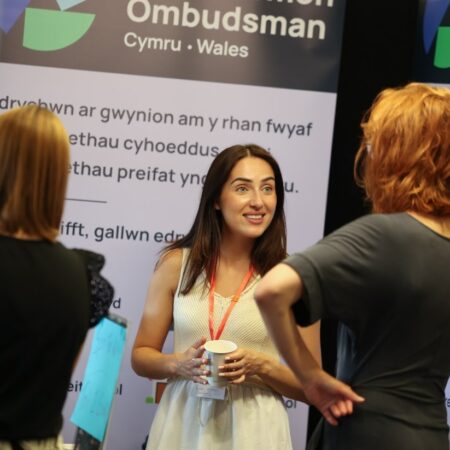 Attendee speaking to another in front of an “Ombudsman Cymru – Wales” display.