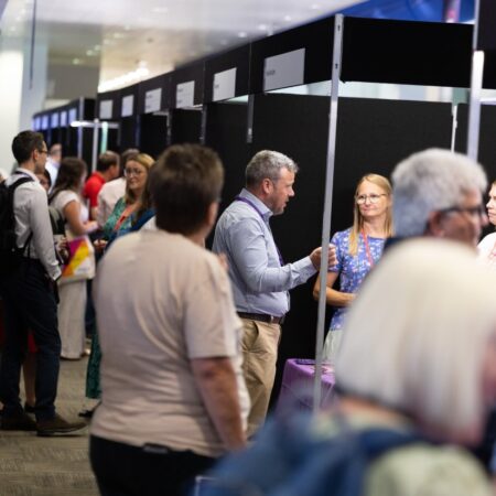 Attendees conversing in an exhibition hall lined with black display panels.